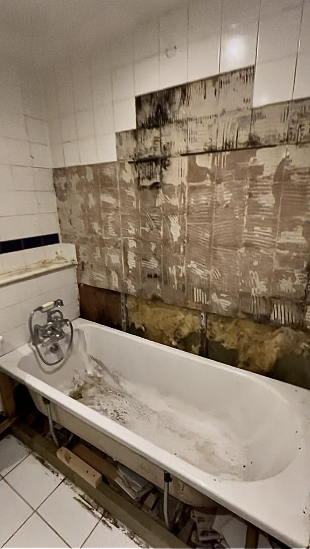 Bathroom wall with tiles removed and damaged plaster before renovation